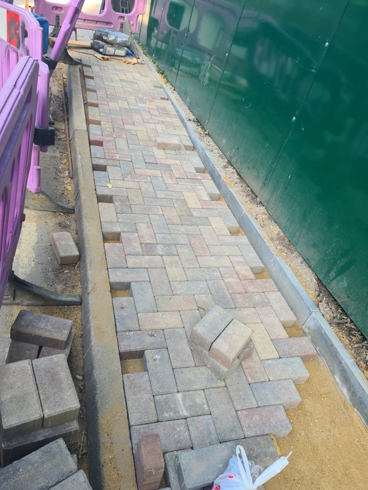 Block paving installation in progress beside site barriers
